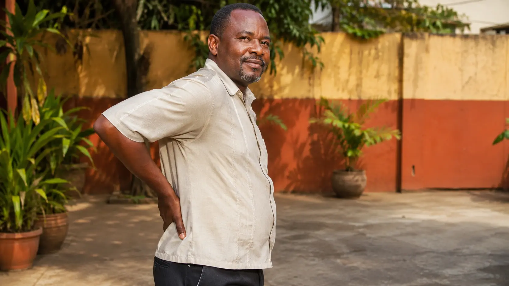 Homme camerounais debout dans une cour à Douala, la main posée sur le bas du dos